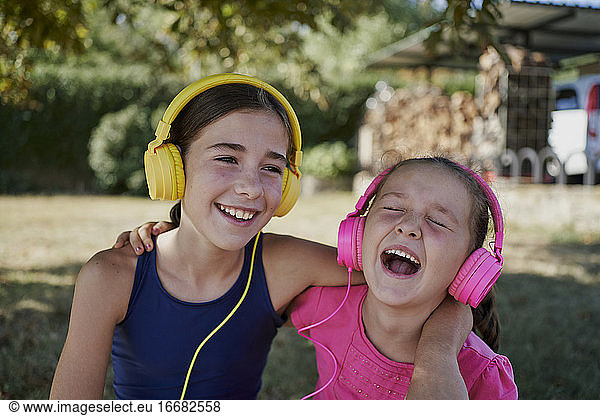 Little girls listening to music and smile with yellow and pink headphones in a garden. happiness concept