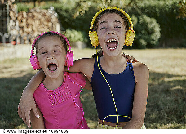 Little girls listening to music and smile with yellow and pink headphones in a garden. happiness concept