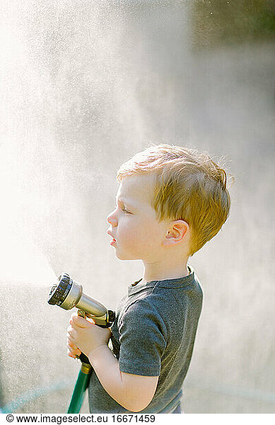 Little toddler boy playing with the garden hose