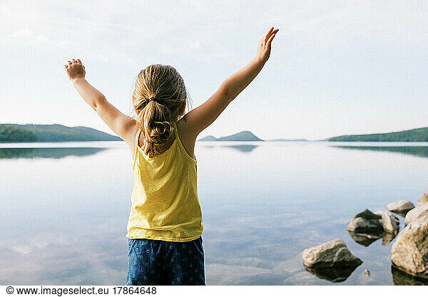 little toddler girl lifting arms with joy by a serene lake