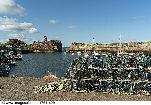 Lobster traps piled along the shore with boats moored in the small  tranquil Victoria harbour at Dunbar  Scotland; Dunbar  East Lothian  Scotland