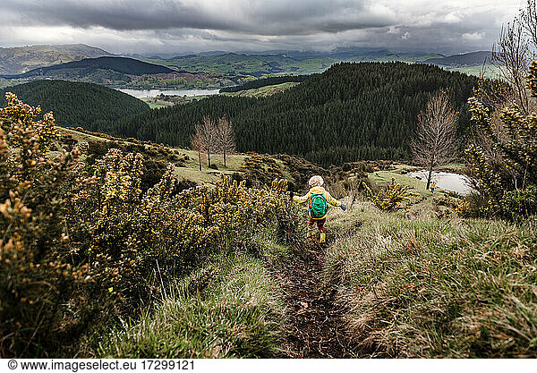 Lockenköpfiger Junge  der mit ausgebreiteten Armen fröhlich auf einem Wanderweg in Neuseeland spazieren geht