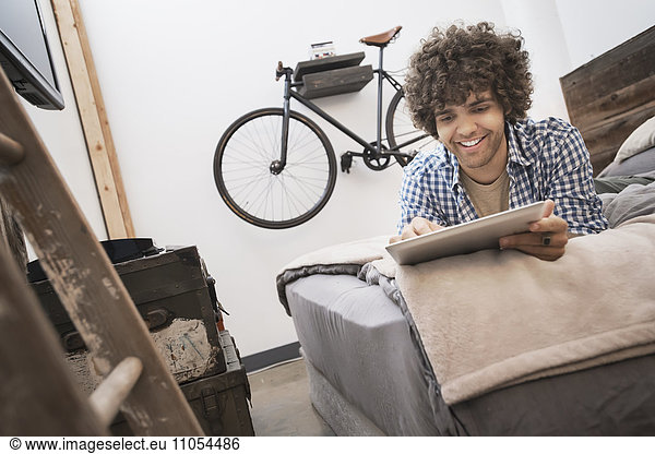 Loft-Wohnen. Ein Fahrrad  das an der Wand hängt. Ein Mann  der ein digitales Tablett benutzt.