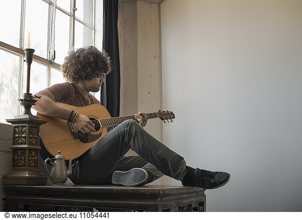 Loft-Wohnen. Ein junger Mann  der am Fenster sitzt und Gitarre spielt.