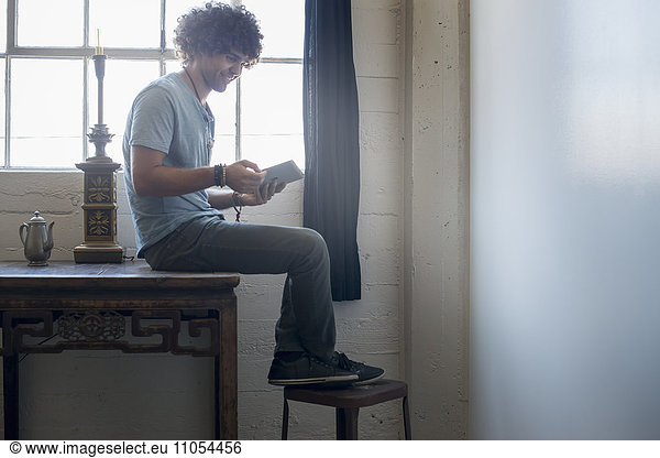 Loft-Wohnen. Ein junger Mann sitzt auf einem Tisch mit einem digitalen Tablett.
