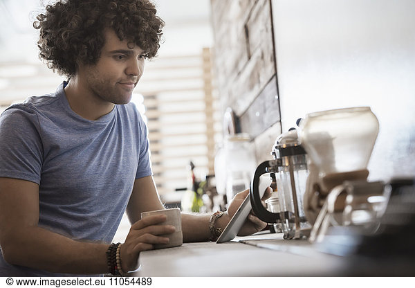 Loft-Wohnen. Ein junger Mann sitzt mit einer Tasse Kaffee und hält ein digitales Tablett in der Hand.