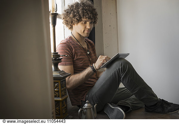 Loft-Wohnen. Ein Mann sitzt am Fenster und benutzt ein digitales Tablett.
