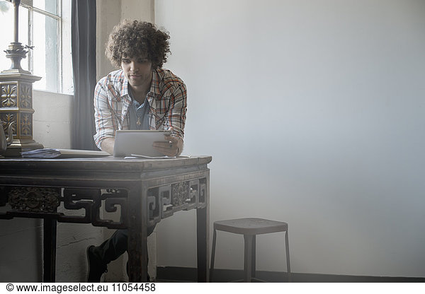 Loft-Wohnen. Ein Mann sitzt an einem Tisch am Fenster und benutzt ein digitales Tablett.