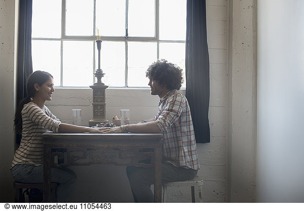Loft-Wohnen. Ein Paar sitzt sich gegenüber und hält sich an den Händen über einen Tisch.