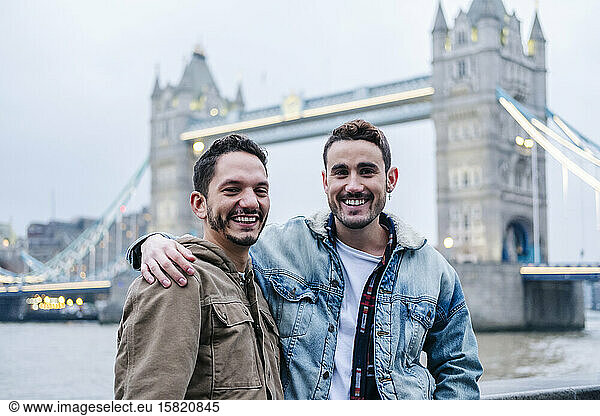 London  United Kingdom  A couple of guysstanding in front of Tower Bridge with arms around