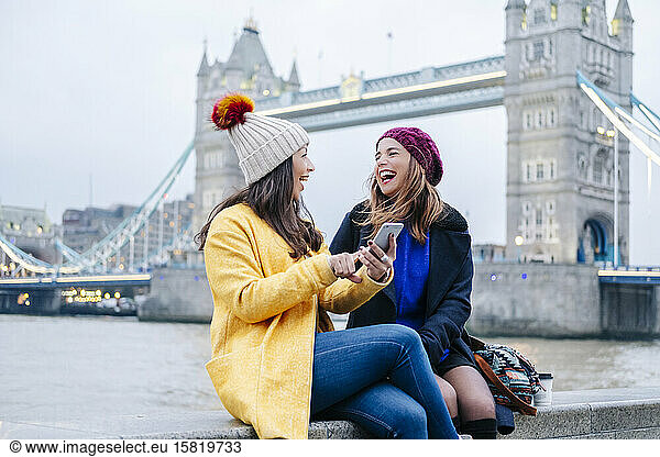 London  United Kingdom  Girlfriends sitting on railing in front of Tower Bridge