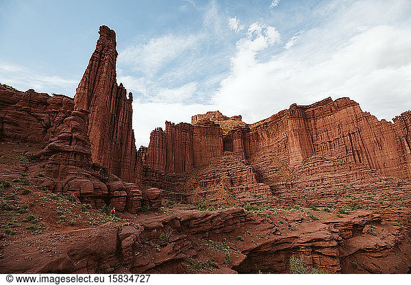 lone hiker under the red rock formation of fisher tower near moab