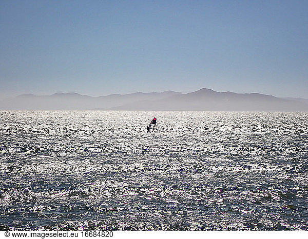 Lone windsurfer sailing across San Francisco bay under blue skis