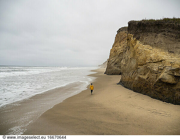 Lone young person walking along deserted California beach on gray day