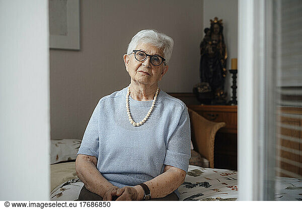 Lonely senior woman sitting on bed in bedroom at home