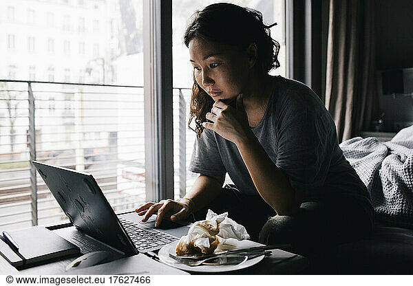 Lonely woman using laptop sitting in bedroom at home