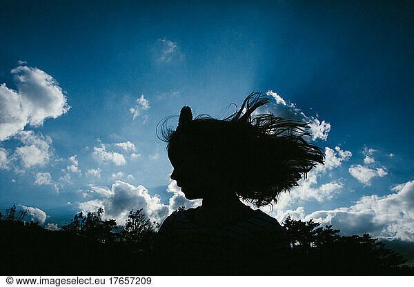 Long hair girl silhouette in front of sunny blue clouds sky