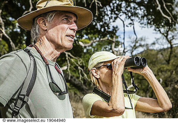 Looking through her binoculars  a husband and wife are out for a day hike.