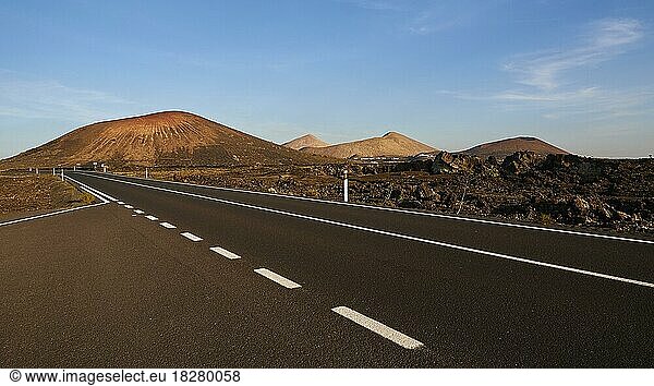 Los Vulcanos  Lava-Landschaften mit vereinzelten Vulkanen  rotbraune Erde  schwarze Asphaltstraße ohne Autos  blauer Himmel  wenige weiße Wolken  Lanzarote  Kanarische Inseln  Spanien  Europa