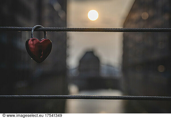 Love lock hanging on bridge railing with setting sun in background