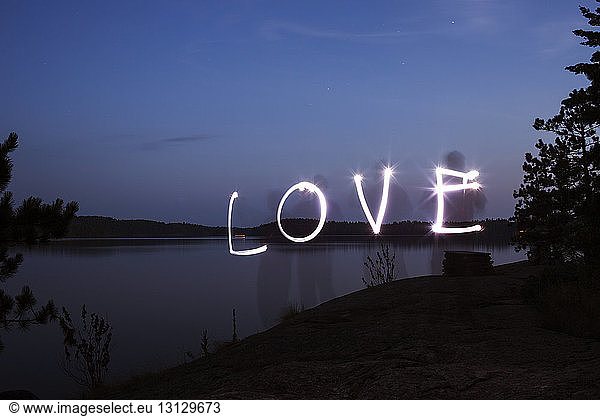 Love text made from light painting over lakeshore against blue sky at dusk