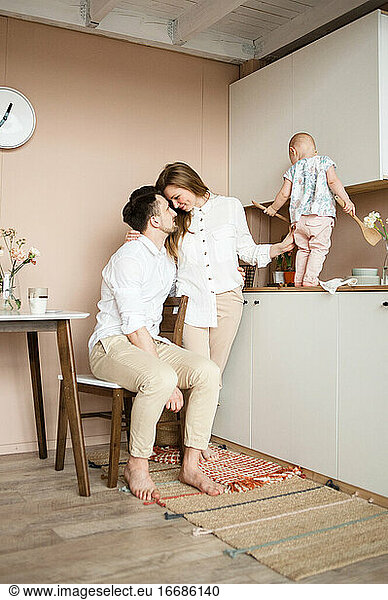 Lovely family of three in kitchen. Mom hugs and looks tender at dad.