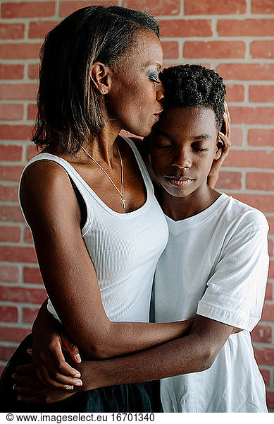 Loving African American mother with closed eyes embraces preteen son