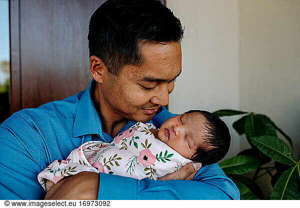 Loving asian dad cradles sleeping newborn baby in his arms
