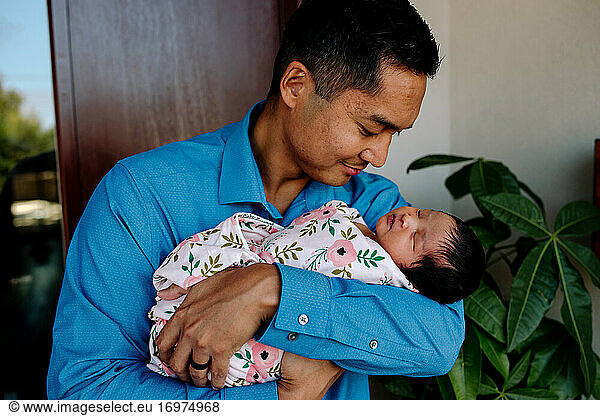 Loving asian father cradles sleeping newborn in his arms