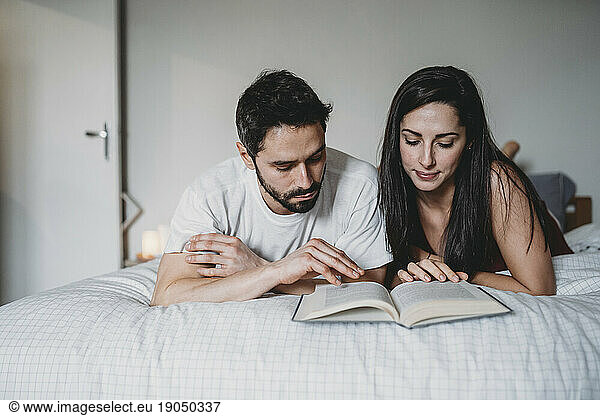 Loving couple reading a book in bed at home in a moment of relax