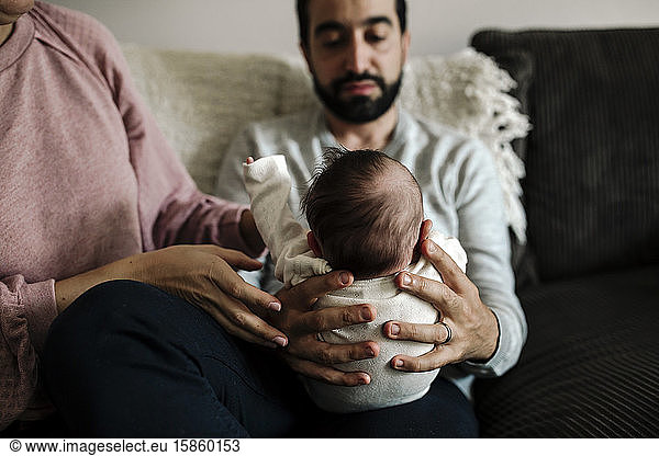 Loving dad with beard holding newborn with gentle touch from wife