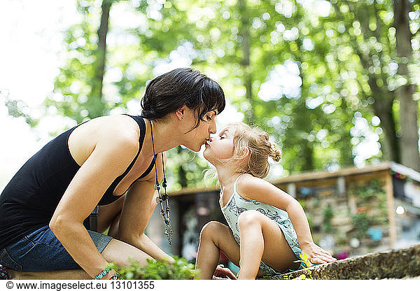 Loving daughter kissing mother on mouth while sitting in backyard