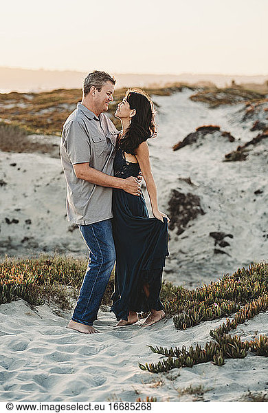 Loving embrace between barefoot mid-40's couple standing in sand
