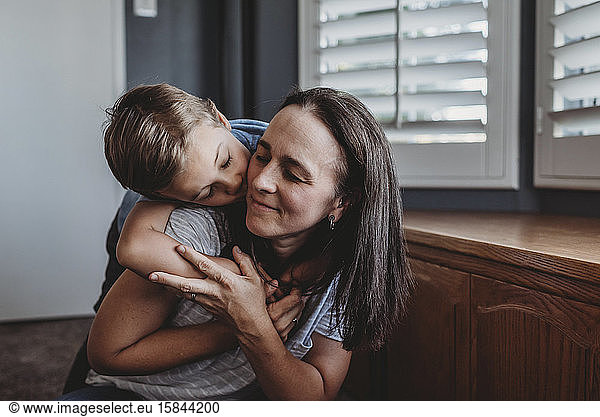 Loving hug between mid-40â€™s mom and 5 yr old son near widow shutters