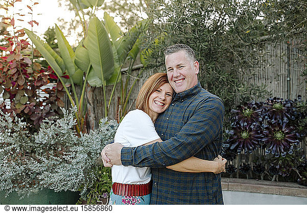 Loving mid-40's husband and wife hugging outdoors near lush plants