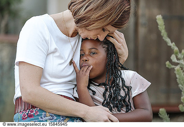 Loving mom holds precious young black daughter with long braids