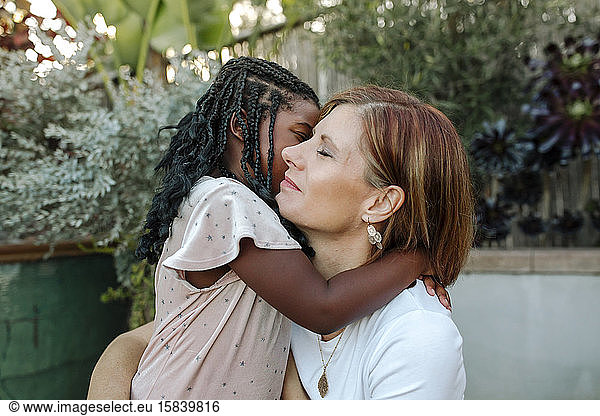 Loving mom hugging young black daughter with long braided hair