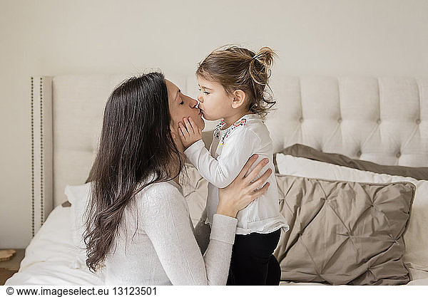 Loving mother and daughter kissing on mouth at home