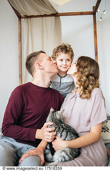 Loving mother and father embrace and kiss baby in cheek