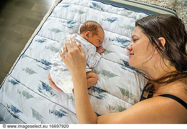 Loving mother gently touching newborn baby laying on stomach.