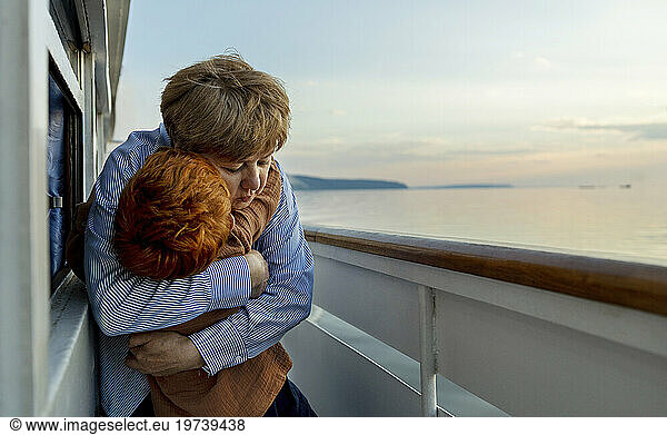 Loving senior woman hugging grandson on ship at dusk