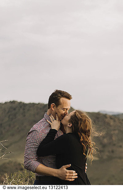 Loving young couple kissing on mouth against sky