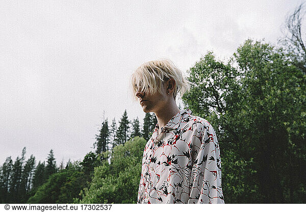 Low Angle of Blonde Teen Standing Against Trees and Sky