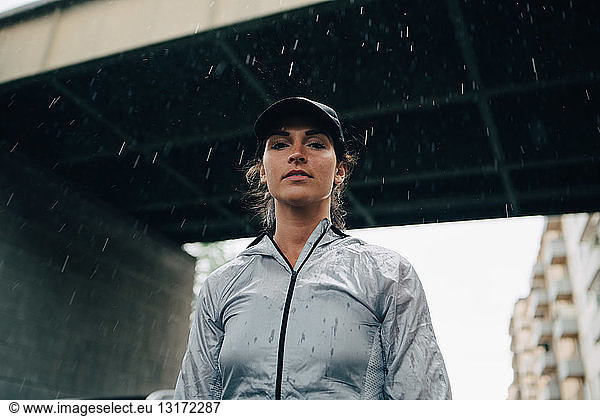 Low angle portrait of female athlete standing against bridge during rainy season