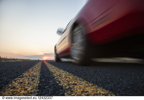 Low angle view looking up at the side of a convertible sports car on the road at sunset.