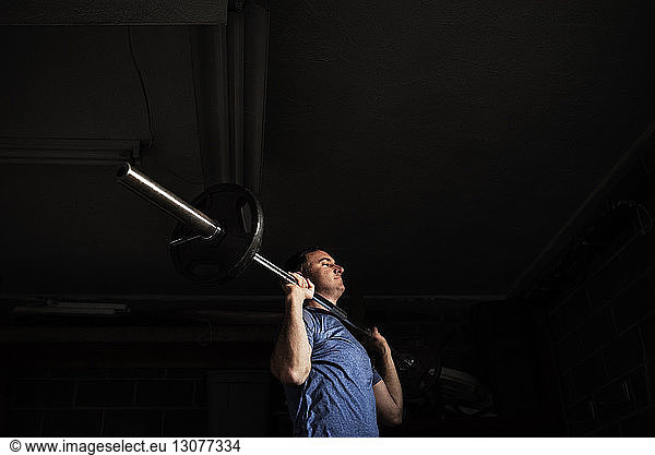 Low angle view of athlete lifting barbell at dark gym