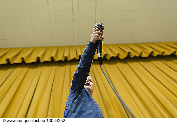 Low angle view of boy holding microphone at stage against yellow curtains
