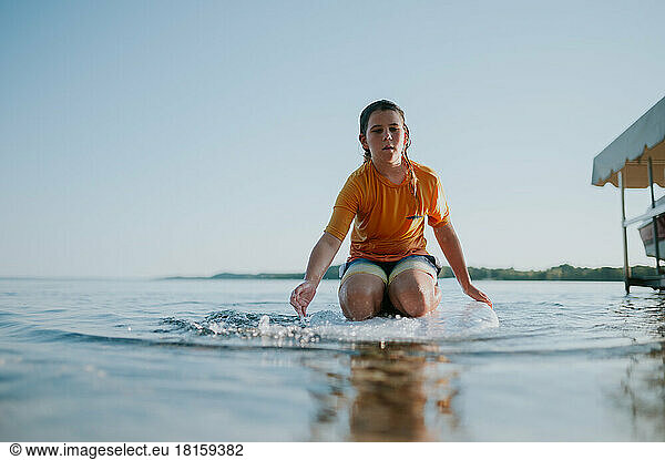 Low angle view of boy sitting on paddle board paddling towards viewer