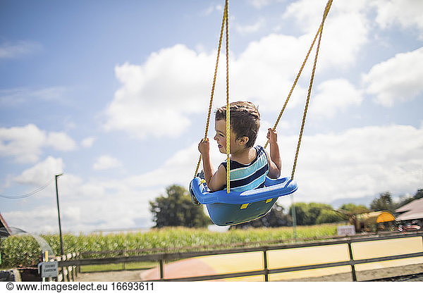 Low angle view of boy swinging outdoors on blue swing at playground.