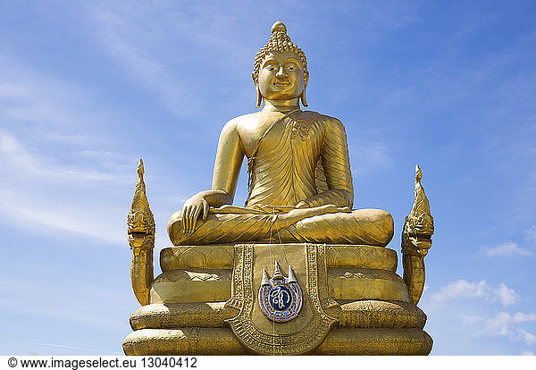 Low angle view of brass Buddha statue against blue sky during sunny day
